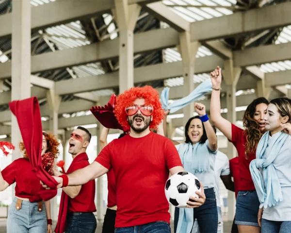 Grupo de aficionados animando con entusiasmo, vestidos con ropa temática y accesorios deportivos, representando la pasión y conexión emocional entre fans y el deporte.