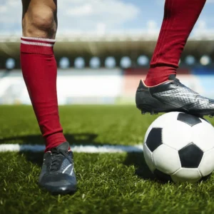 Piernas de jugadores de fútbol en un campo de césped, con un balón bajo uno de los pies, simbolizando el dinamismo y la conexión del deporte.