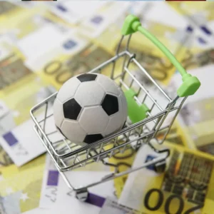 Carrito de compras con un balón de fútbol dentro, colocado sobre billetes de euro, simbolizando la economía y los patrocinios en el marketing deportivo.