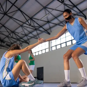 Chica levantando a su compañera de equipo durante un partido de balonmano, mostrando apoyo y trabajo en equipo en un momento de esfuerzo y colaboración.