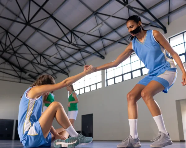 Chica levantando a su compañera de equipo durante un partido de balonmano, mostrando apoyo y trabajo en equipo en un momento de esfuerzo y colaboración.